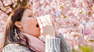 Allergie und Heuschnupfen: Frau nießt unter blühenden Bäumen
