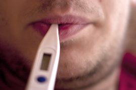 Erkältung mit Fieber, Mann mit Fieberthermometer