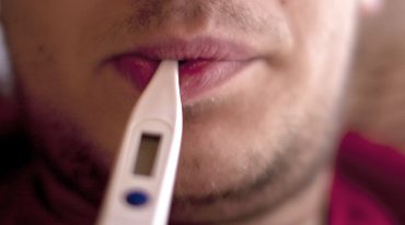 Erkältung mit Fieber, Mann mit Fieberthermometer