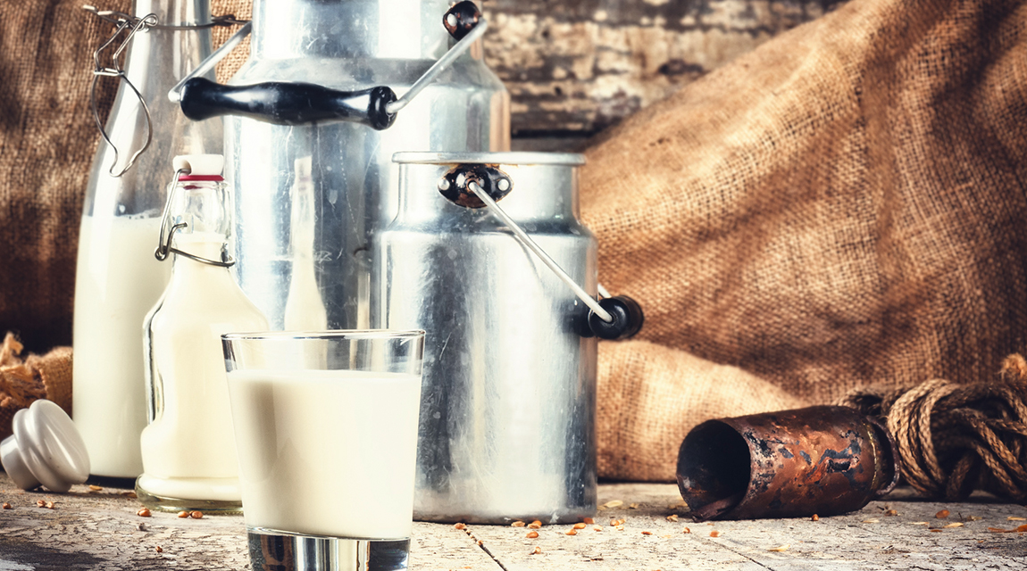Laktoseintoleranz: frische Milch im Glas und in Milchkannen