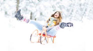 glückliche Frau fährt Schlitten durch den Schnee