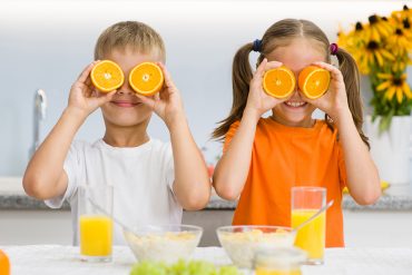 Happy kids holds orange before his eyes like in glasses.