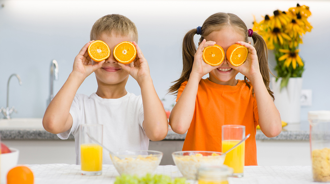 Happy kids holds orange before his eyes like in glasses.