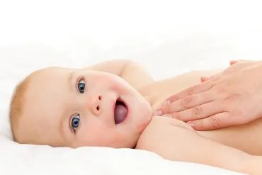 Baby wird mit Pflegeöl massiert und grinst